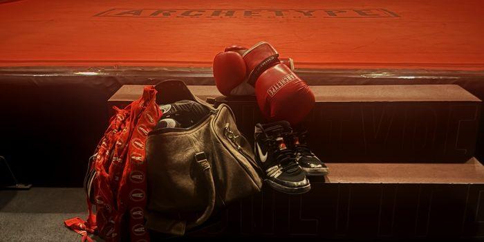 Archetype boxing gloves, wraps, gym bag, and boxing shoes resting on the steps of the ring