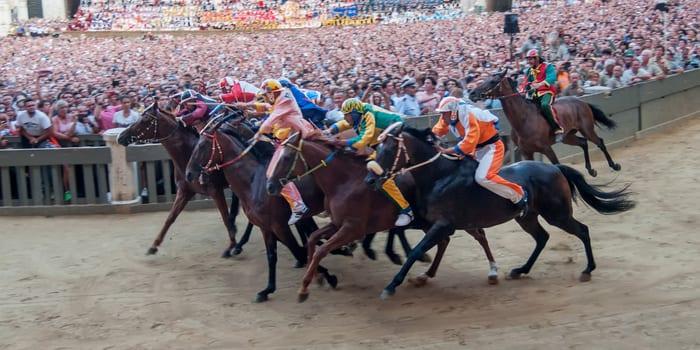 Horses and jockeys racing before a packed crowd at the Palio di Siena